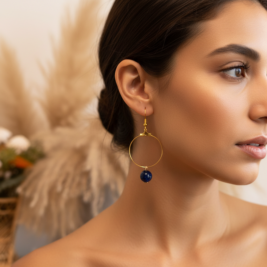 Boucles créoles dorées, perle bleue marine pendante, portées sur l’oreille