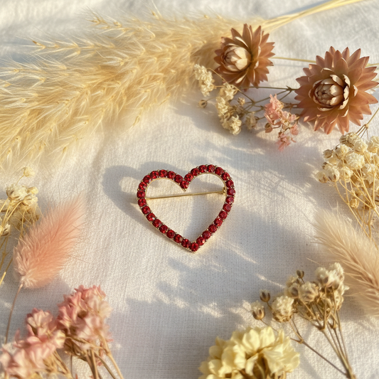 Broche cœur dorée avec strass rouges scintillants.