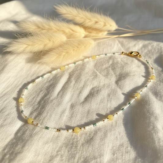 Collier de perles bleu clair et jaunes, fermoir doré, posé sur tissu clair