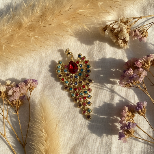 Broche paon dorée multicolore avec pierre rouge, détail floral en forme de plume