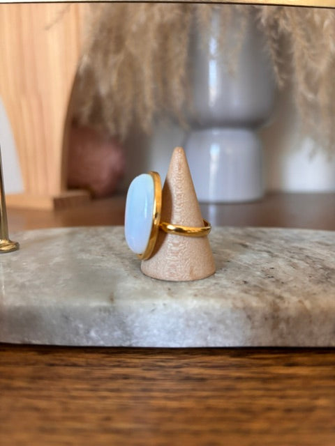 Bague dorée ajustable avec cabochon opaline ovale bleu, vue de profil sur support