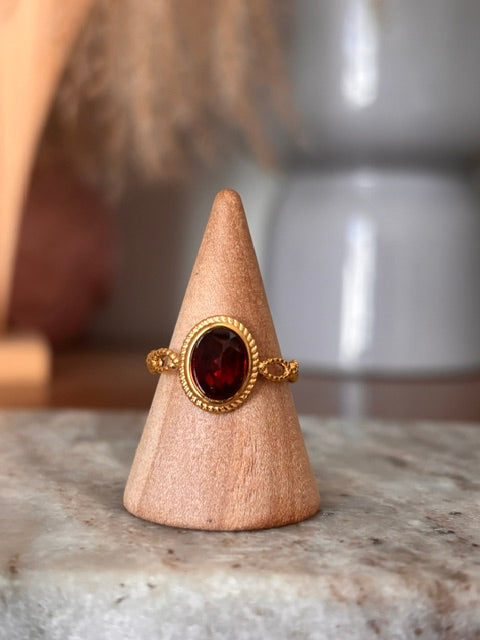 Bague dorée ajustable avec cabochon grenat ovale serti dans un motif vintage.