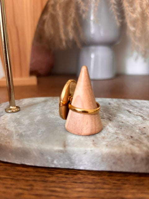 Bague cabochon ovale plume de paon avec anneau doré, vue côté sur fond rose