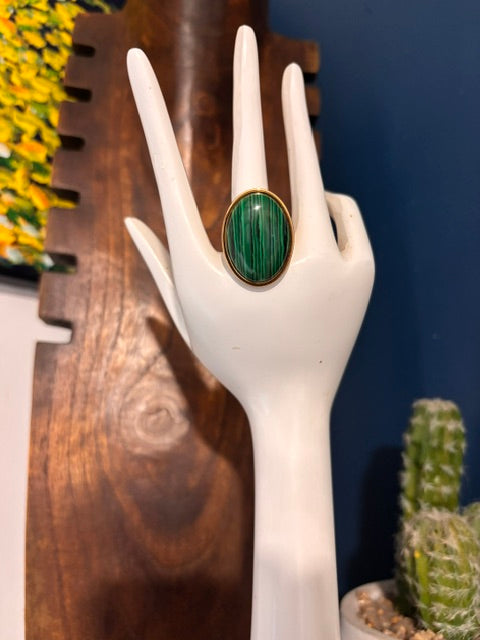 Bague dorée avec cabochon ovale de Malachite verte présentée sur un support blanc