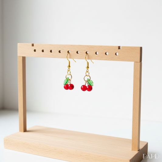Boucles d’oreilles cerises rouges pendantes, crochets dorés, sur présentoir en bois