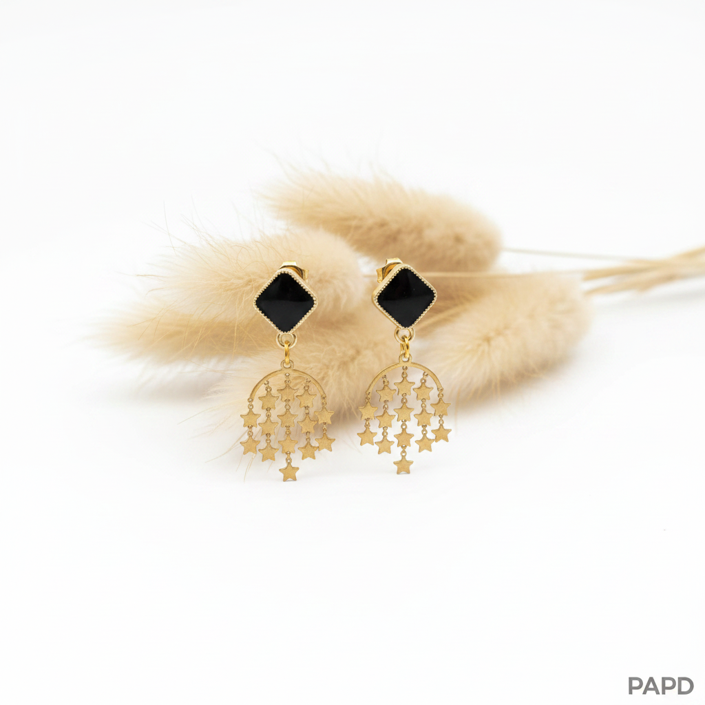 Boucles d’oreilles dorées avec pastille noire et pendentifs en forme d’étoiles ajourées.