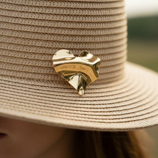 Broche cœur doré froissé brillante sur chapeau à bord large en paille.