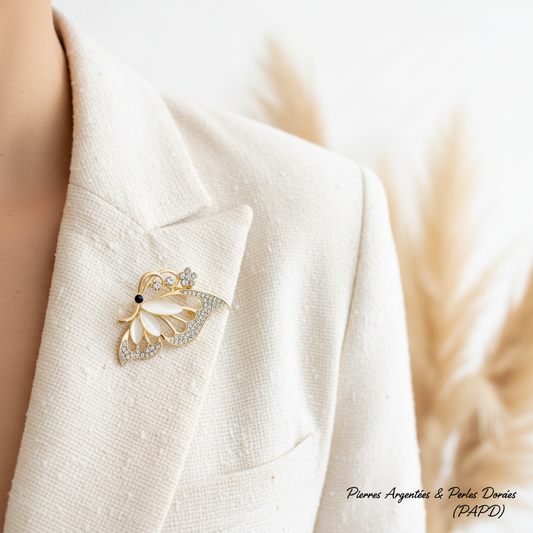 Broche papillon doré et argenté sur veste claire, ailes à strass et perles.