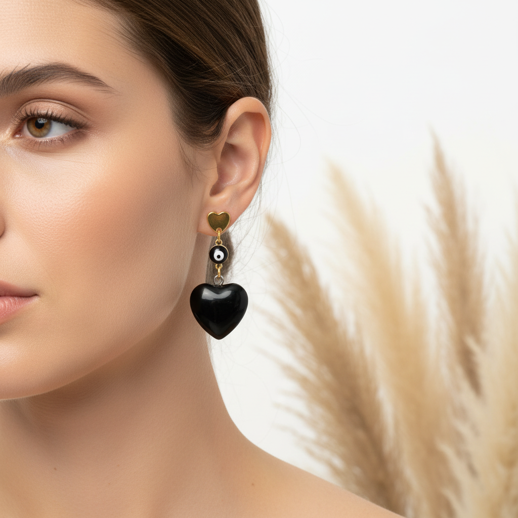 Boucle d’oreille pendante dorée avec cœur noir et petit motif œil, vue de profil.