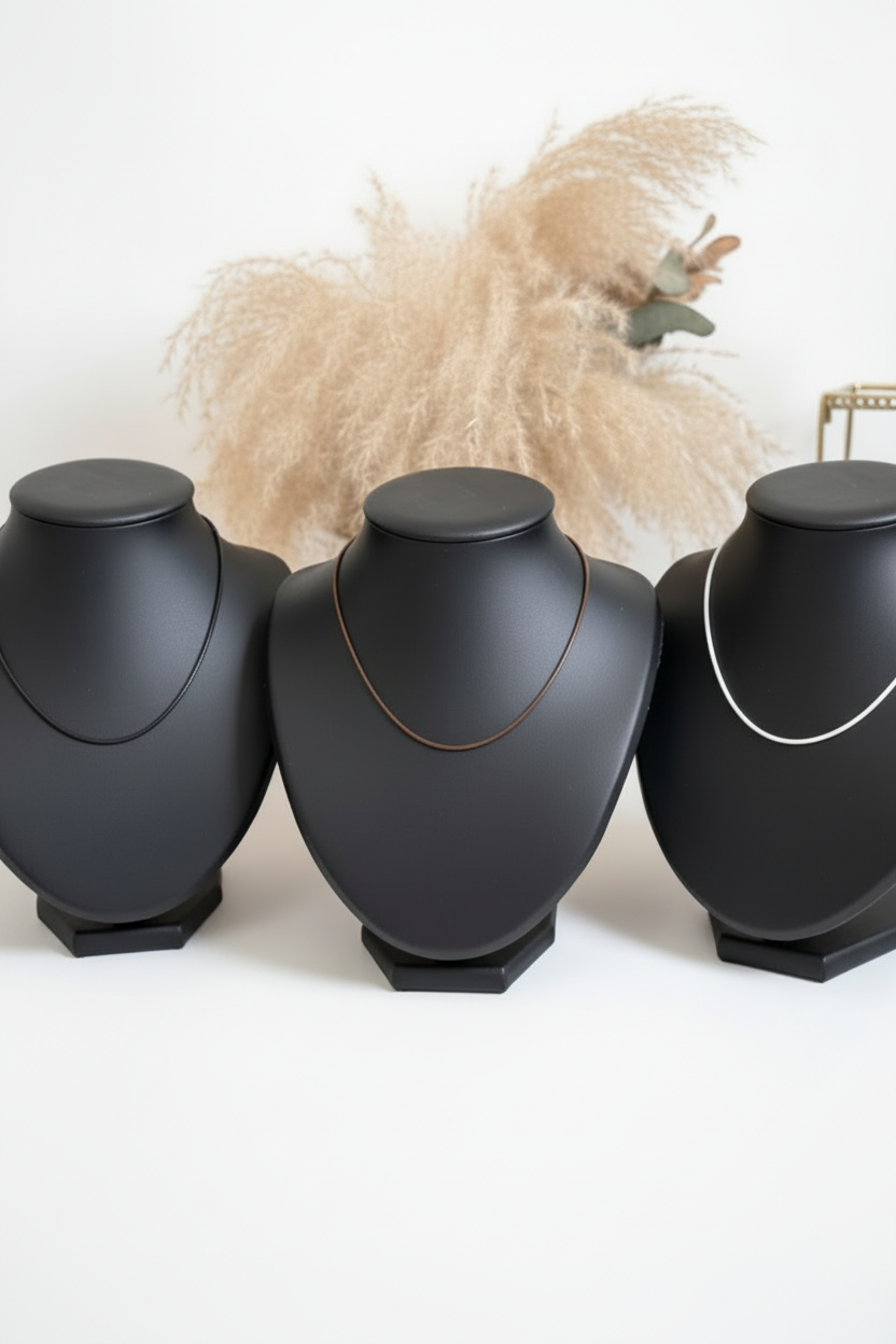 Trois cordons de collier en simili cuir noir, marron et blanc présentés seuls sur trois bustes, sans chaînettes d’extension visibles