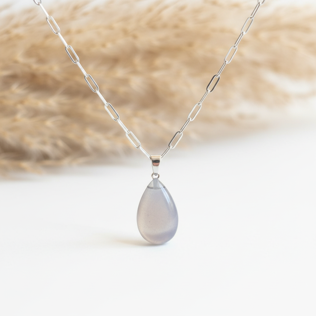 Gros plan d’un pendentif goutte en pierre de Lune naturelle grise et gris perle, avec bélière argentée et chaîne gourmette argentée